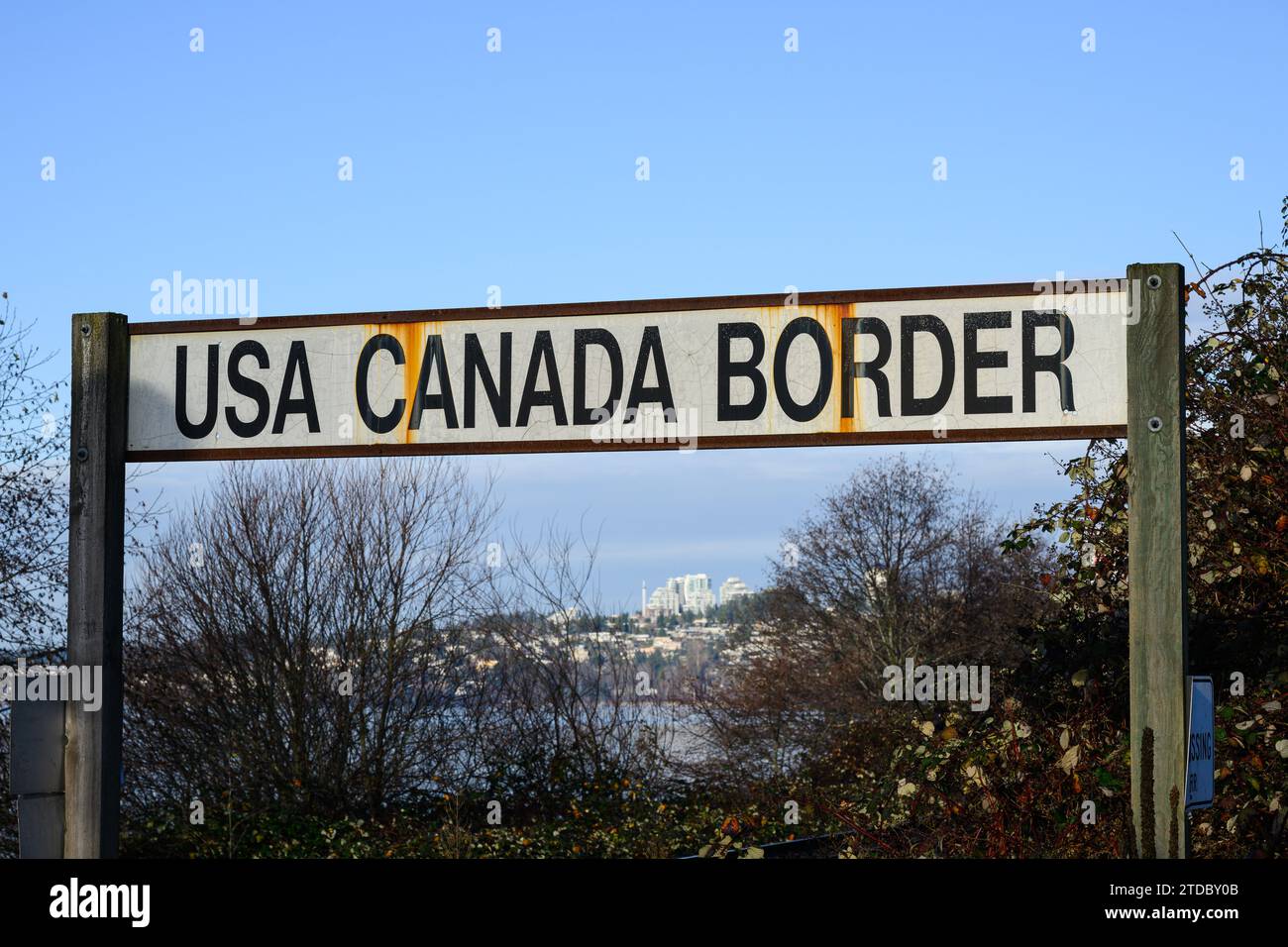 Textschild in schwarzen Großbuchstaben auf weißem Hintergrund für USA Kanada-Grenze mit Rostspuren vom Metallrahmen Stockfoto