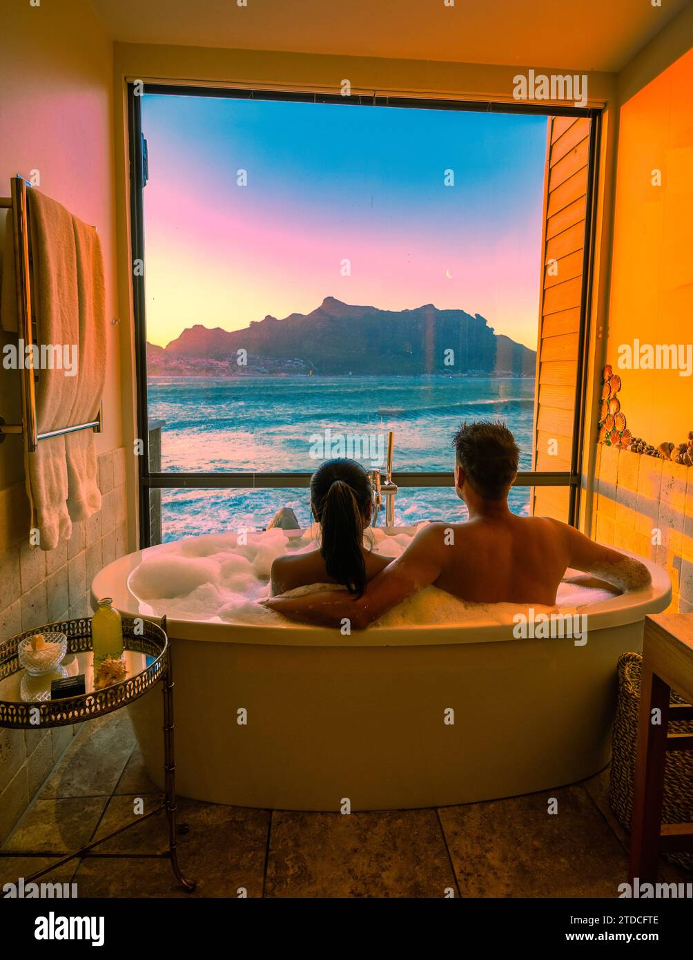 Ein vielfältiges Paar Männer und Frauen in der Badewanne mit Blick auf das Meer von Kapstadt Südafrika während des Urlaubs. Badewanne bei Sonnenuntergang, Mann und Frau aus verschiedenen Rassen in der Badewanne im Urlaub Stockfoto