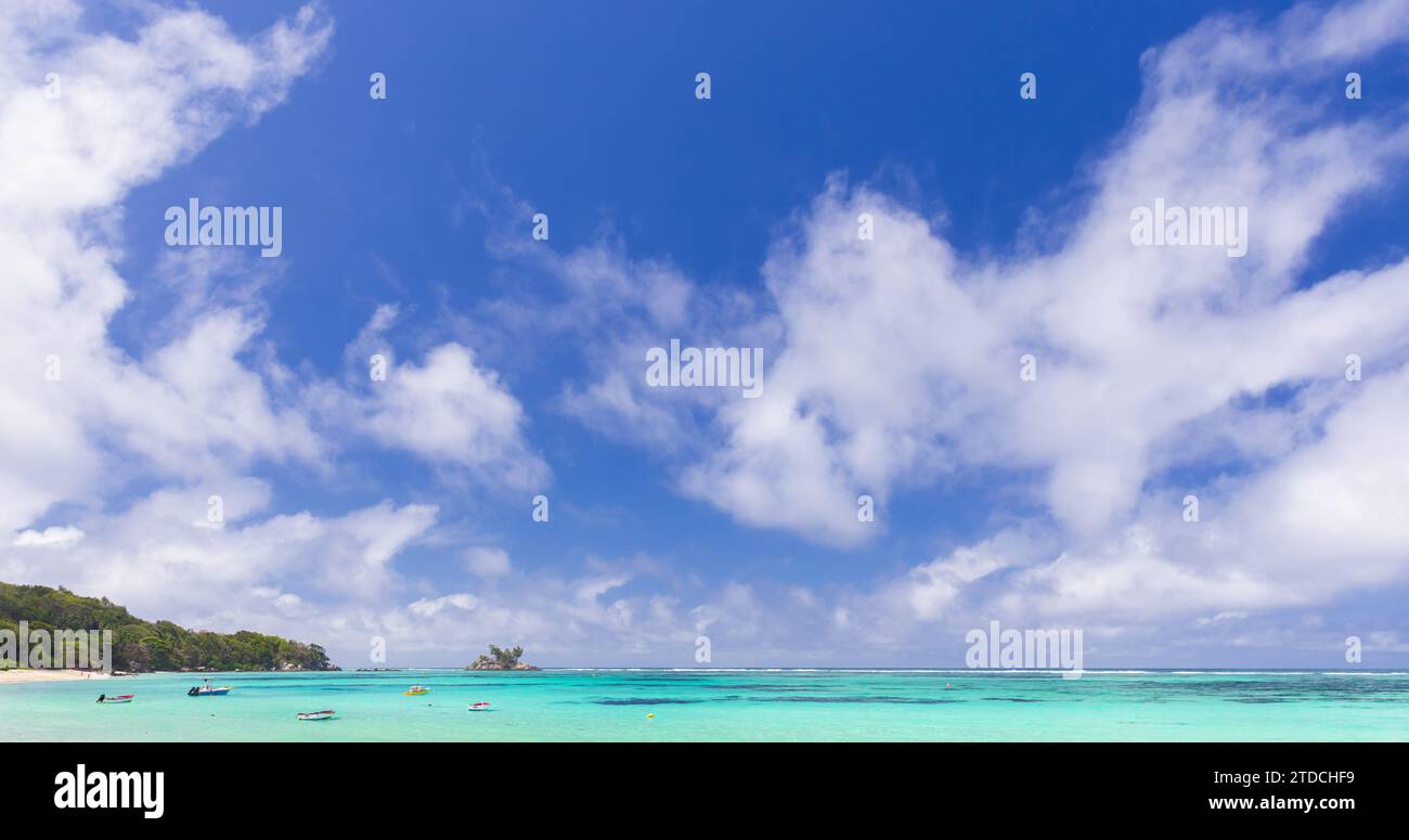 Anse Royale, Seychellen. Blick auf die Küste mit kleinen Booten unter blauem Himmel mit weißen Wolken an einem sonnigen Tag Stockfoto