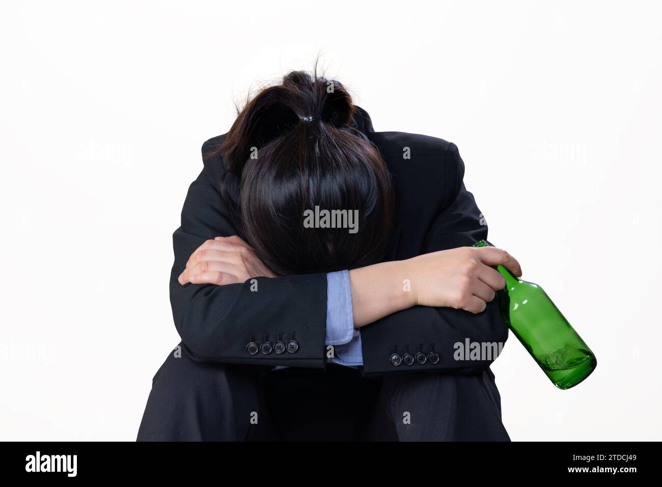 Eine verzweifelte Frau, die eine Flasche Alkohol mit dem Kopf nach unten vor einem weißen Hintergrund hält Stockfoto