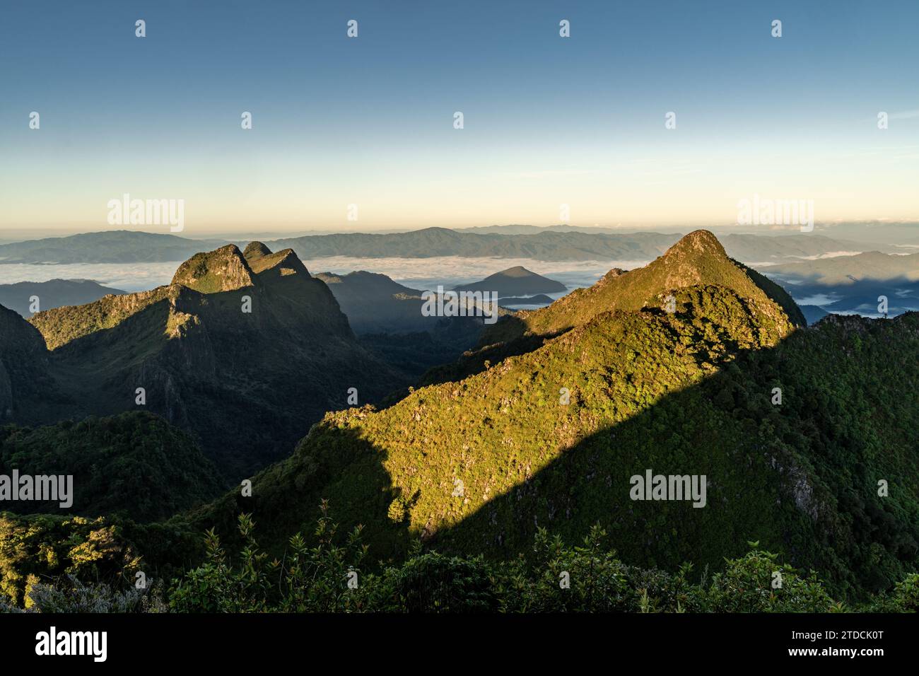 Blick von der Spitze des Doi Luang Chiang Dao während eines Morgensonnenaufgangs mit Bäumen und Sträuchern im Vordergrund und wunderschönen Bergketten im Hintergrund Stockfoto