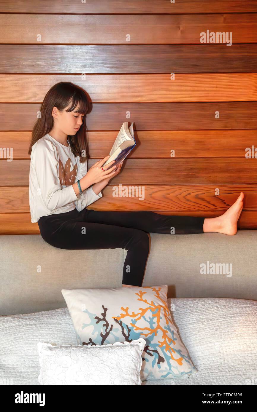 Das elfjährige Mädchen liest ein Buch auf einem Bettkopfteil Stockfoto