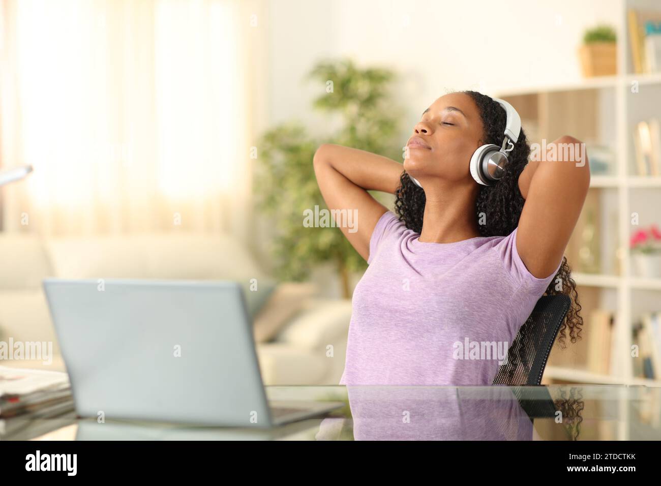 Schwarze Frau hört Audio mit Kopfhörern, die sich zu Hause entspannen Stockfoto