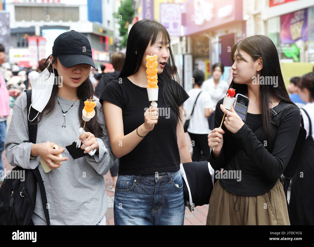 Studentinnen gehen zu Fuß, während sie Tanghulu, einen traditionellen chinesischen Snack, auf einer Straße in Korea essen Stockfoto