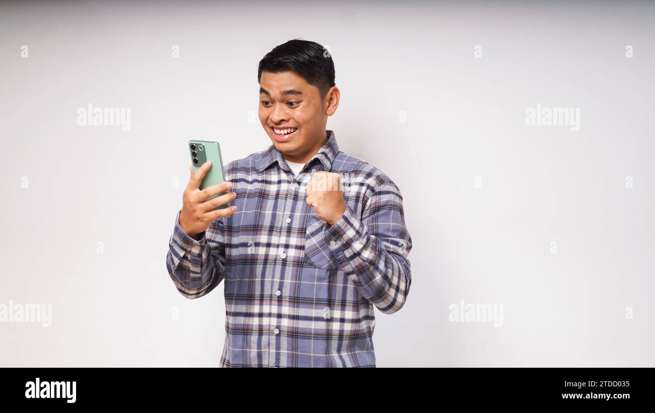 Junger asiatischer Mann, der ein Handy hält und enthusiastischen Ausdruck zeigt Stockfoto