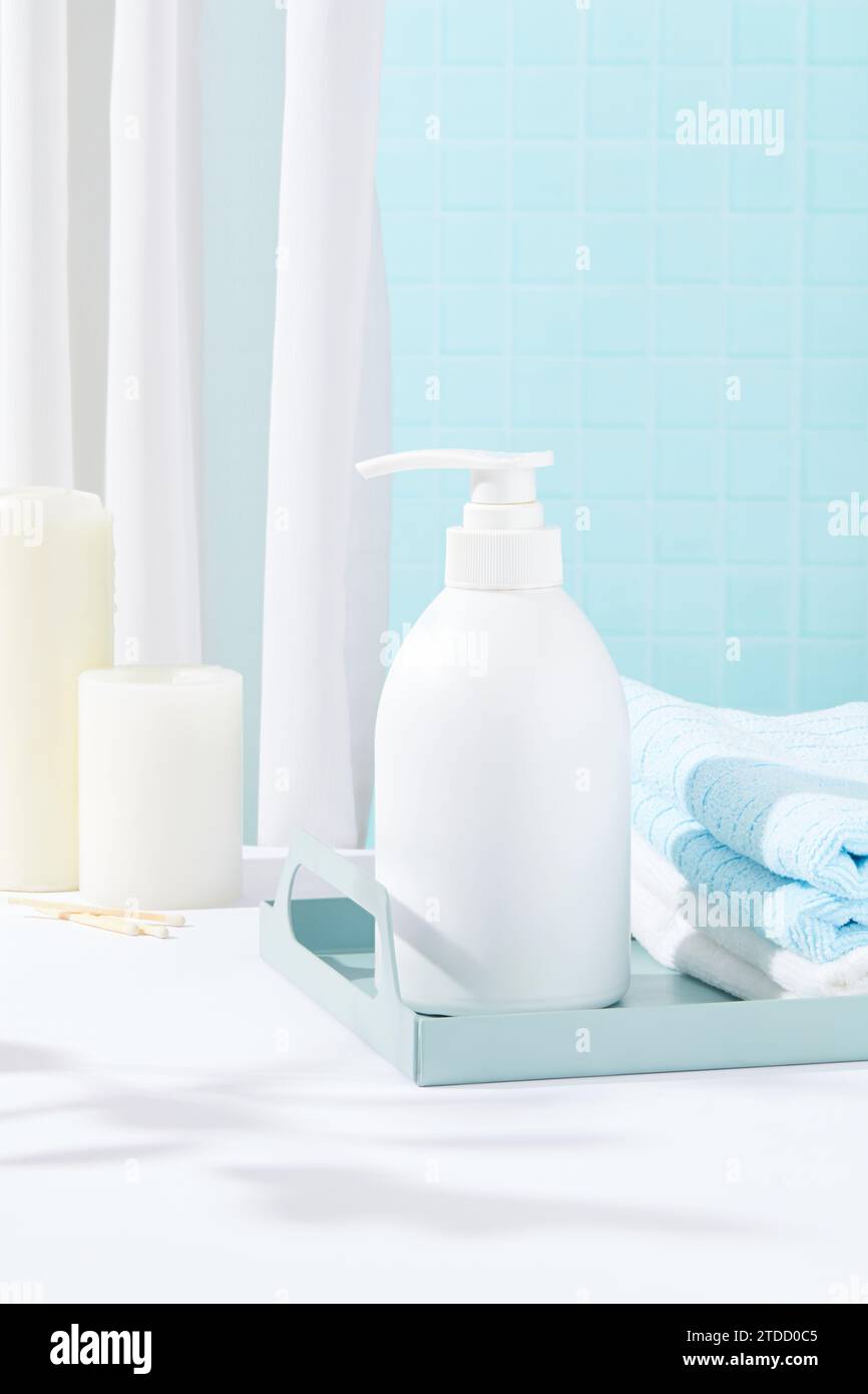 Gefaltete Handtücher und eine Flasche weißes Duschgel befinden sich auf einem Tablett. Weißer Tisch mit Kerzen. Eleganter Raum mit zwei Hauptfarben: Stockfoto