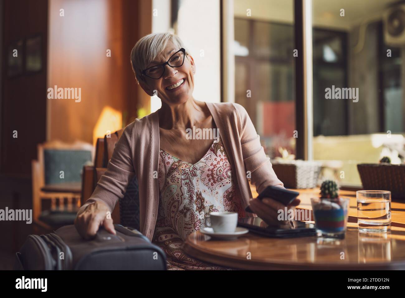 Reife Frau sitzt in einem Café am Flughafen und wartet auf das Boarding. Stockfoto