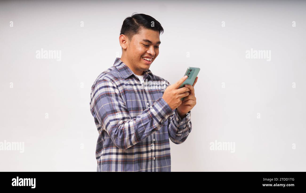 Junger asiatischer Mann, der ein Handy hält und enthusiastischen Ausdruck zeigt Stockfoto