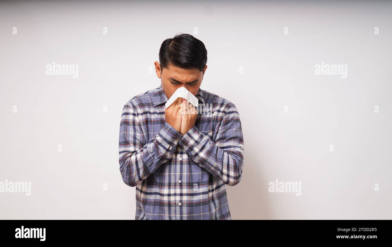 Junger erwachsener asiatischer Mann bedeckt Nase und Mund mit Gewebe, wenn er auf weißem Hintergrund niest. studio-Aufnahme Stockfoto