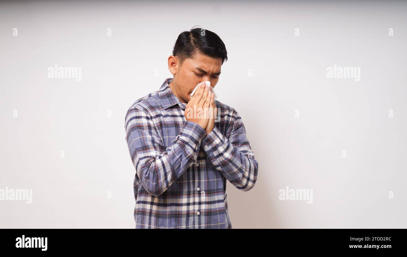 Junger erwachsener asiatischer Mann bedeckt Nase und Mund mit Gewebe, wenn er auf weißem Hintergrund niest. studio-Aufnahme Stockfoto