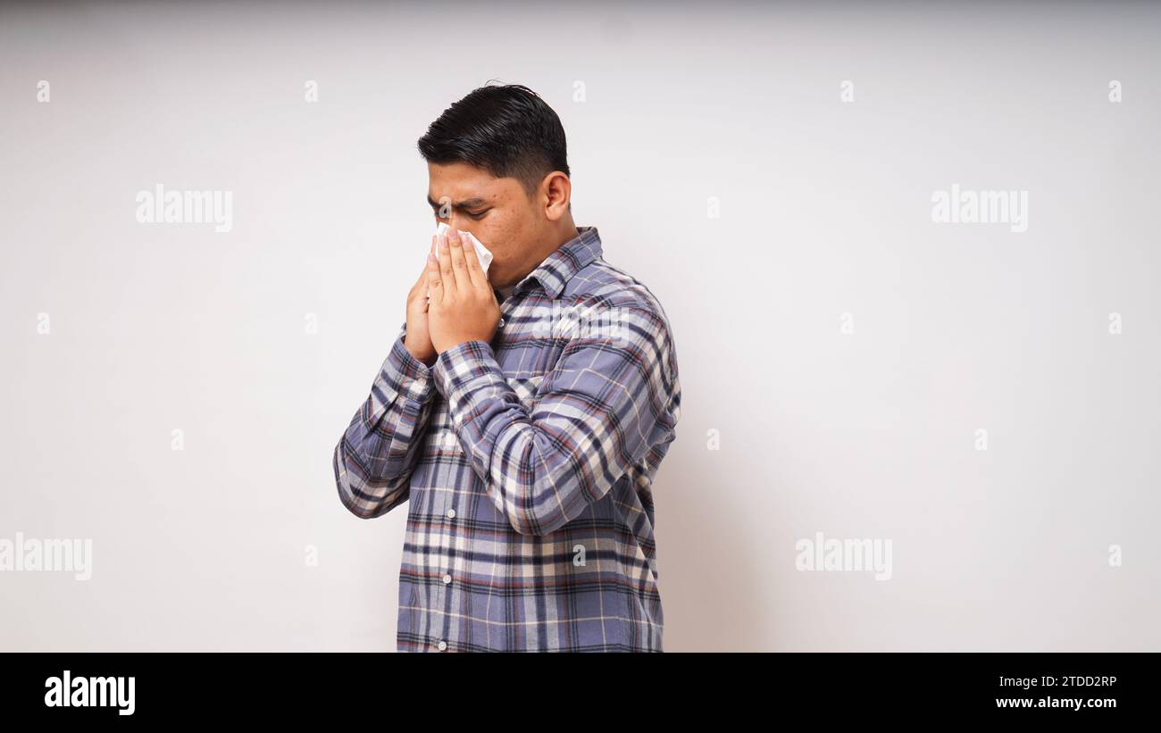 Junger erwachsener asiatischer Mann bedeckt Nase und Mund mit Gewebe, wenn er auf weißem Hintergrund niest. studio-Aufnahme Stockfoto