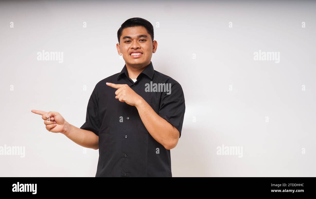 Junger asiatischer Mann lächelt, wenn er auf weißem Hintergrund nach rechts zeigt. studio-Aufnahme Stockfoto