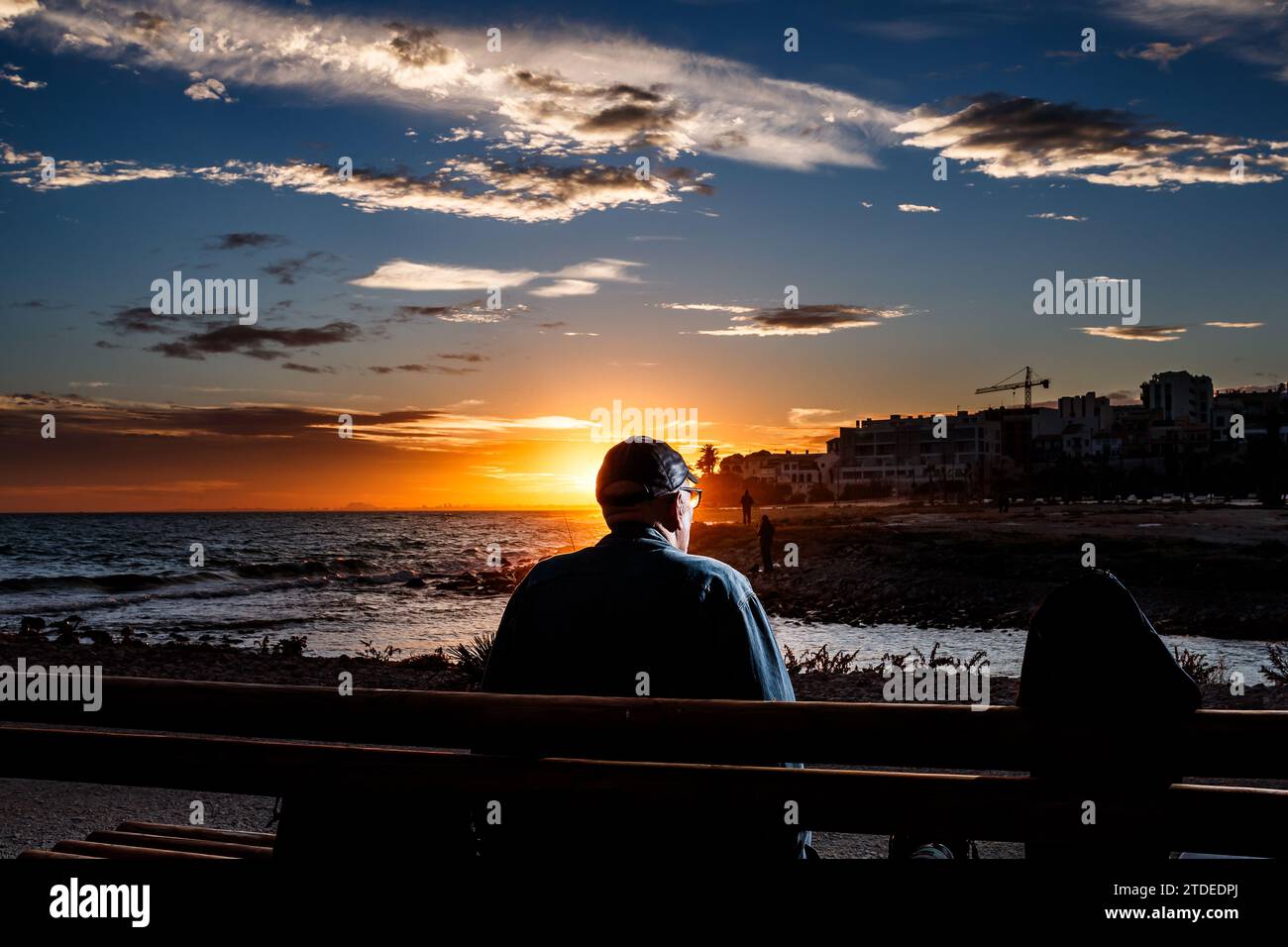 Ruhiger Mann, der auf einer Bank sitzt und den Sonnenuntergang beobachtet Stockfoto