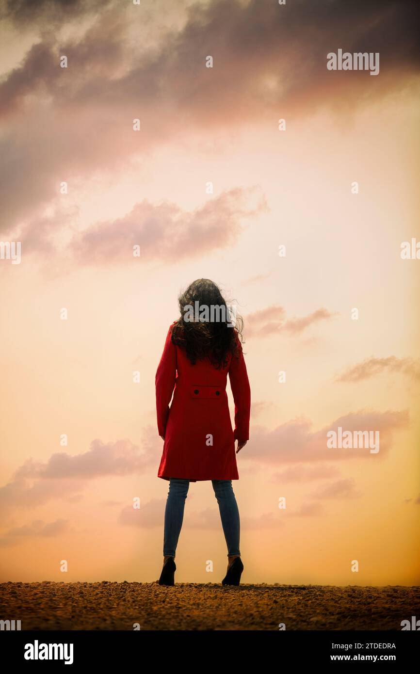 Rückansicht einer Frau im roten Mantel, die bei Sonnenuntergang draußen steht Stockfoto