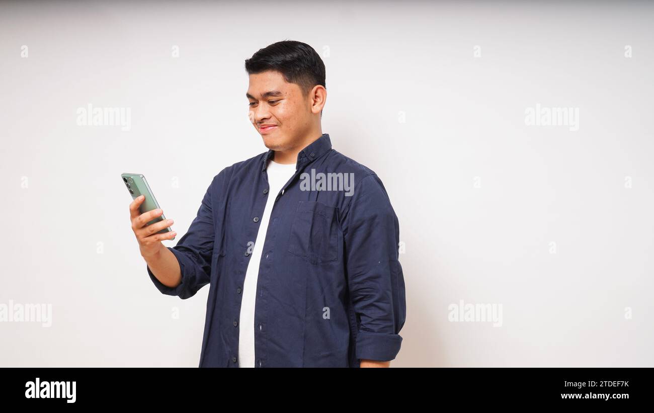 Junger asiatischer Mann, der ein Handy hält und enthusiastischen Ausdruck zeigt Stockfoto