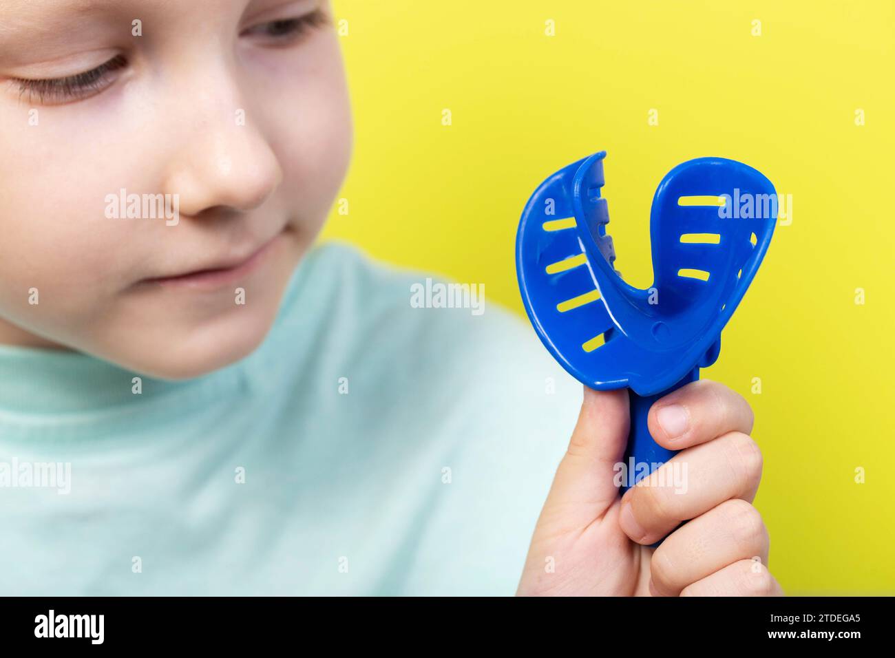 Ein siebenjähriges Mädchen schaut sich in der Kieferorthopädie ein blaues Abdrucktablett an. Konzept zur Herstellung von Zahnspangen und Prothesen für Kinder, Korrektur o Stockfoto