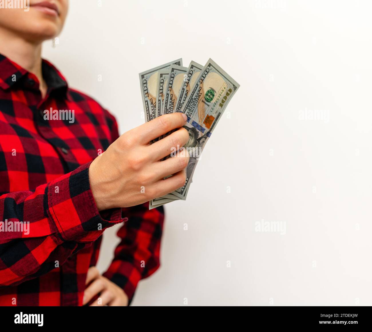 Frau mit lässigem rotem kariertem Hemd, die Dollarscheine in der Hand vor weißem Hintergrund hält. Geldtransfer, Geldwechsel. Stockfoto