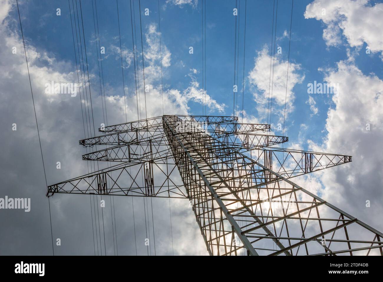 Strommast und Stromleitungen mit blauem Himmel und ersten Gewitterwolken im Hintergrund Stockfoto