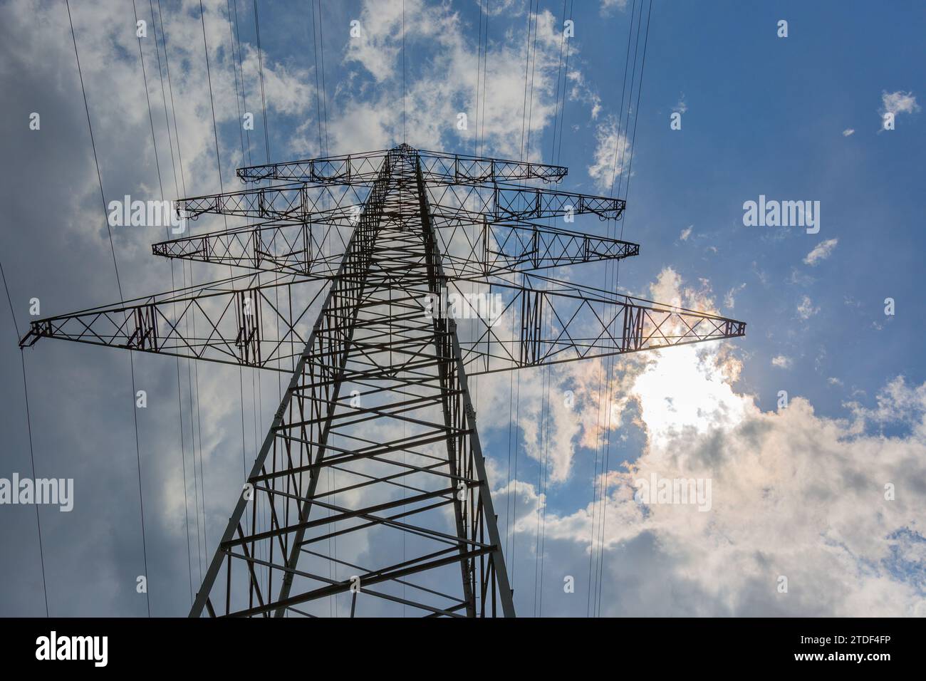 Strommast und Stromleitungen mit blauem Himmel und ersten Gewitterwolken im Hintergrund Stockfoto