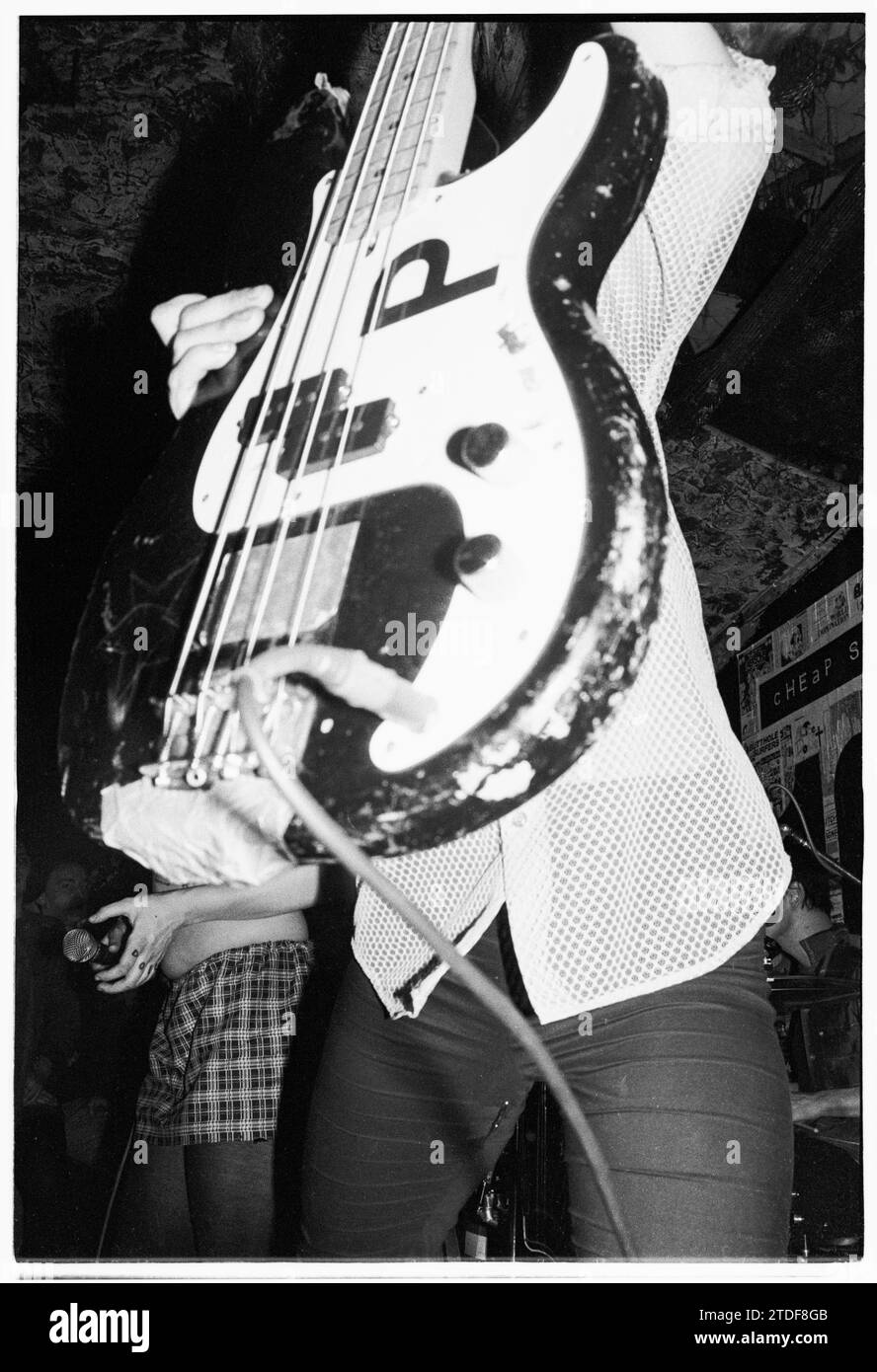 KATHLEEN HANNA, BIKINI KILL, NEWPORT TJS, 1993: Kathleen Hanna, die Sängerin von Bikini Kill, versteckt die Band mit ihrer Bassgitarre am 8. März 1993 bei den legendären TJs in Newport, Wales, Großbritannien vor der Kamera. Diese Bikini Kill/Huggy Bear Tour kam auf dem Höhepunkt der Riot Grrrl Szene und sollte die beiden Bands kombiniertes Album Yeah Yeah Yeah Yeah Yeah (Kill Rock Stars) aus dem Jahr 1993 bewerben. Der Auftritt begann mit einem Musikworkshop nur für Frauen. Foto: Rob Watkins Stockfoto