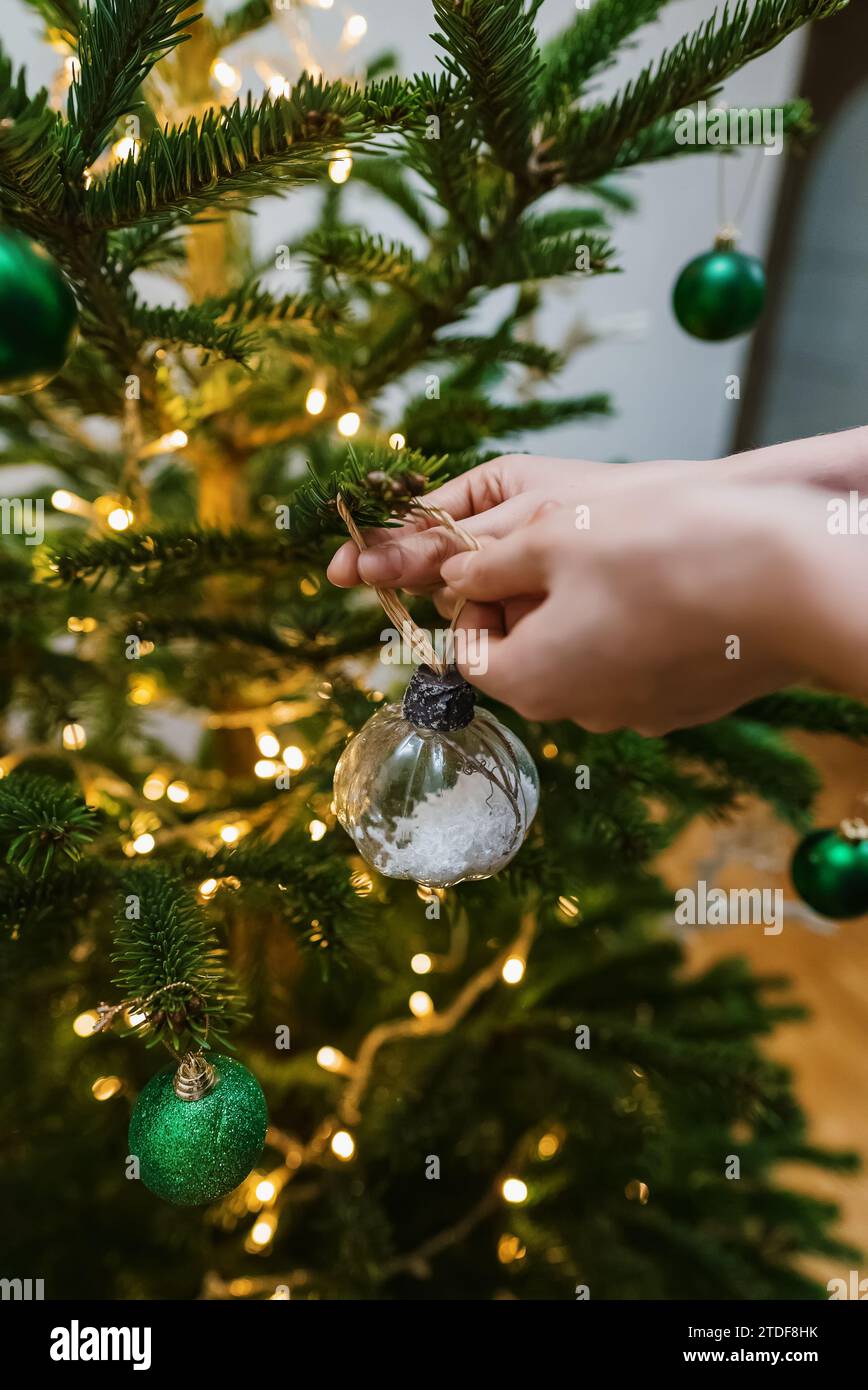 Eine Frau hängt einen Ball an einem Neujahrsbaum. Stockfoto