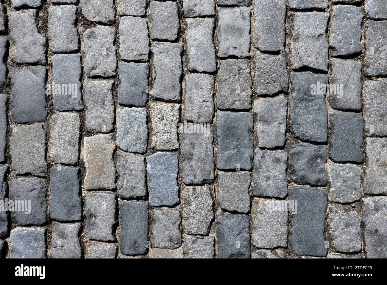 Dunkelgraues Kopfsteinpflaster aus alten glatten Steinen als Hintergrund von oben Stockfoto