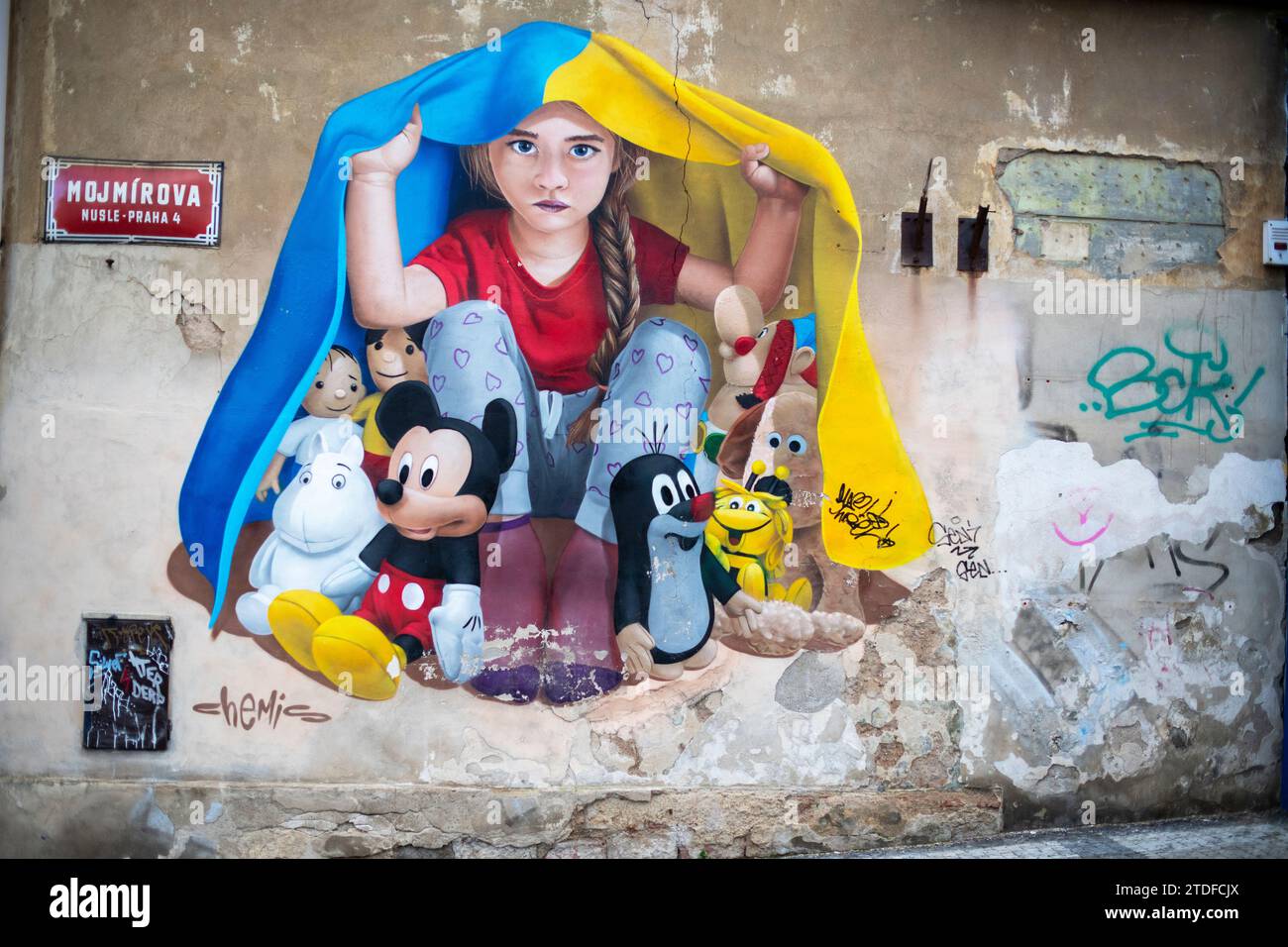 Ein Wandbild eines jungen Mädchens, das unter ukrainischer Flagge in Prag Zuflucht sucht. Wandgemälde Street Art von Chemis Stockfoto