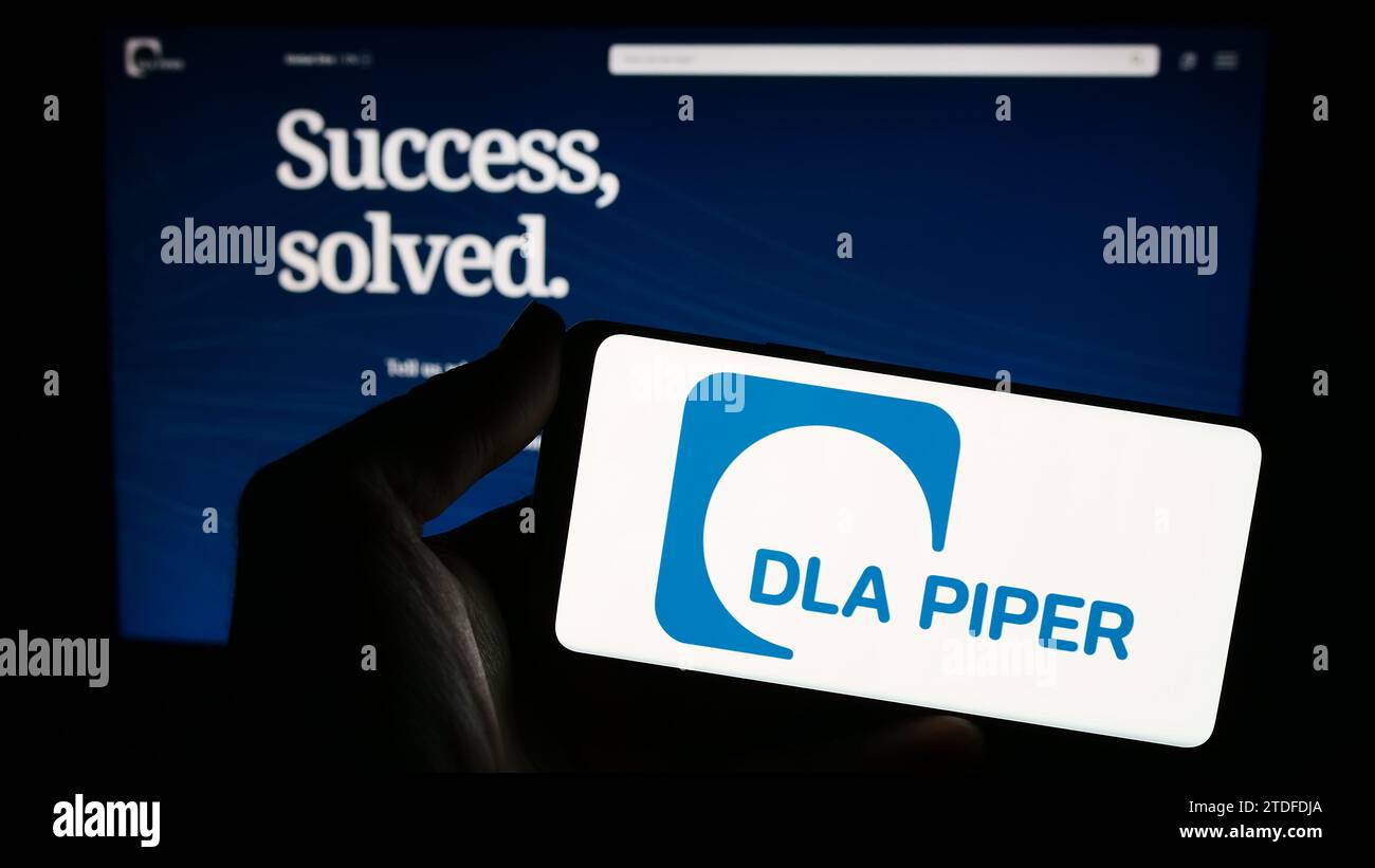 Person mit Smartphone und Logo der Anwaltskanzlei DLA Piper vor der Website. Schwerpunkt auf dem Display des Telefons. Stockfoto