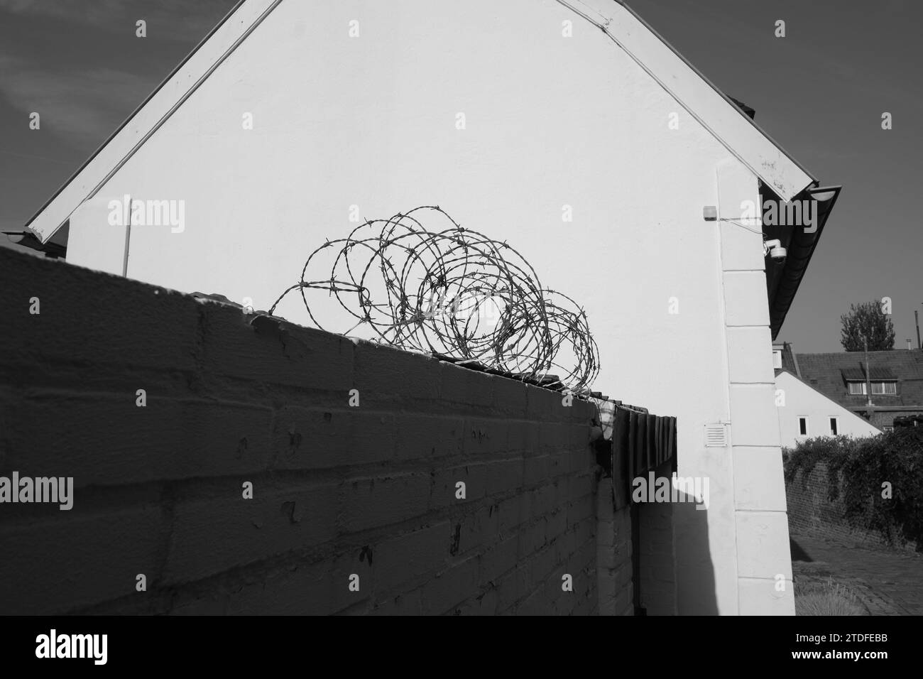 Stacheldraht auf einer Ziegelmauer mit einem whte-Haus daneben Stockfoto