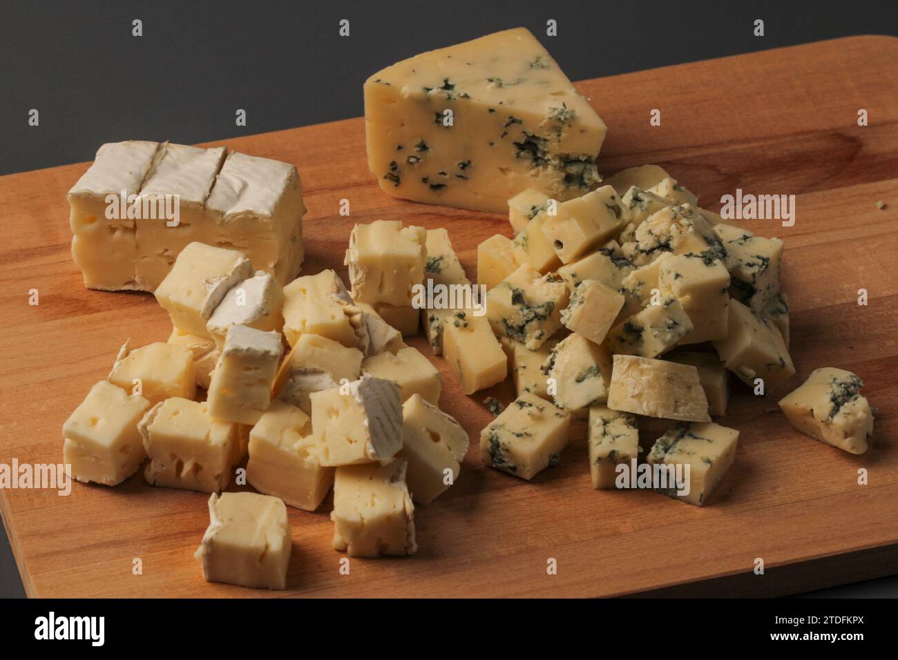 In Scheiben geschnittene Käsestücke auf einem Holzbrett auf grauem Hintergrund Stockfoto