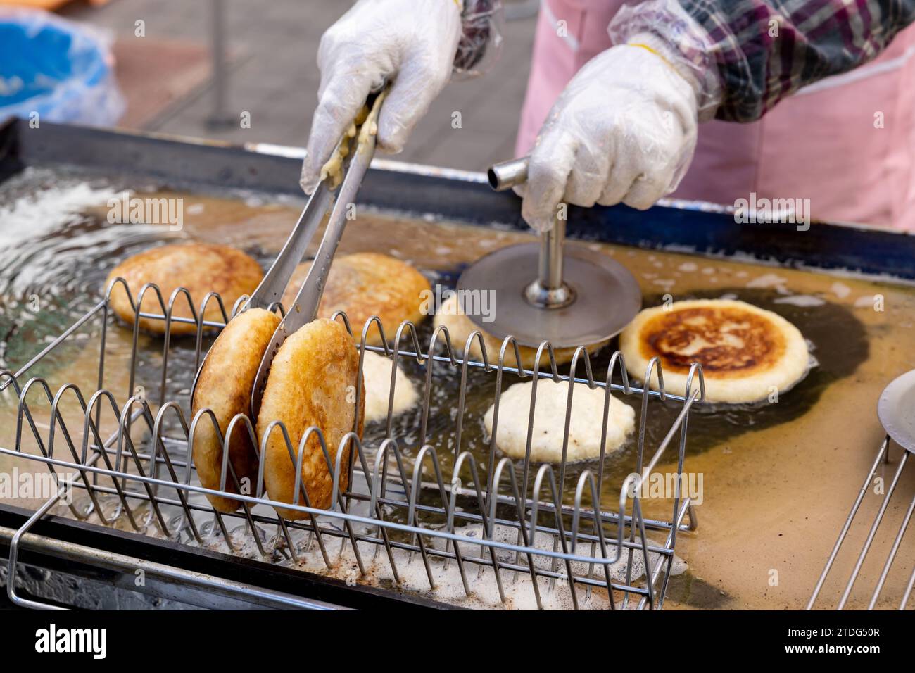 Hotteok zum Verkauf und die Hände eines Händlers, der es auf einer Straße auf einem traditionellen Markt in Korea grillt Stockfoto