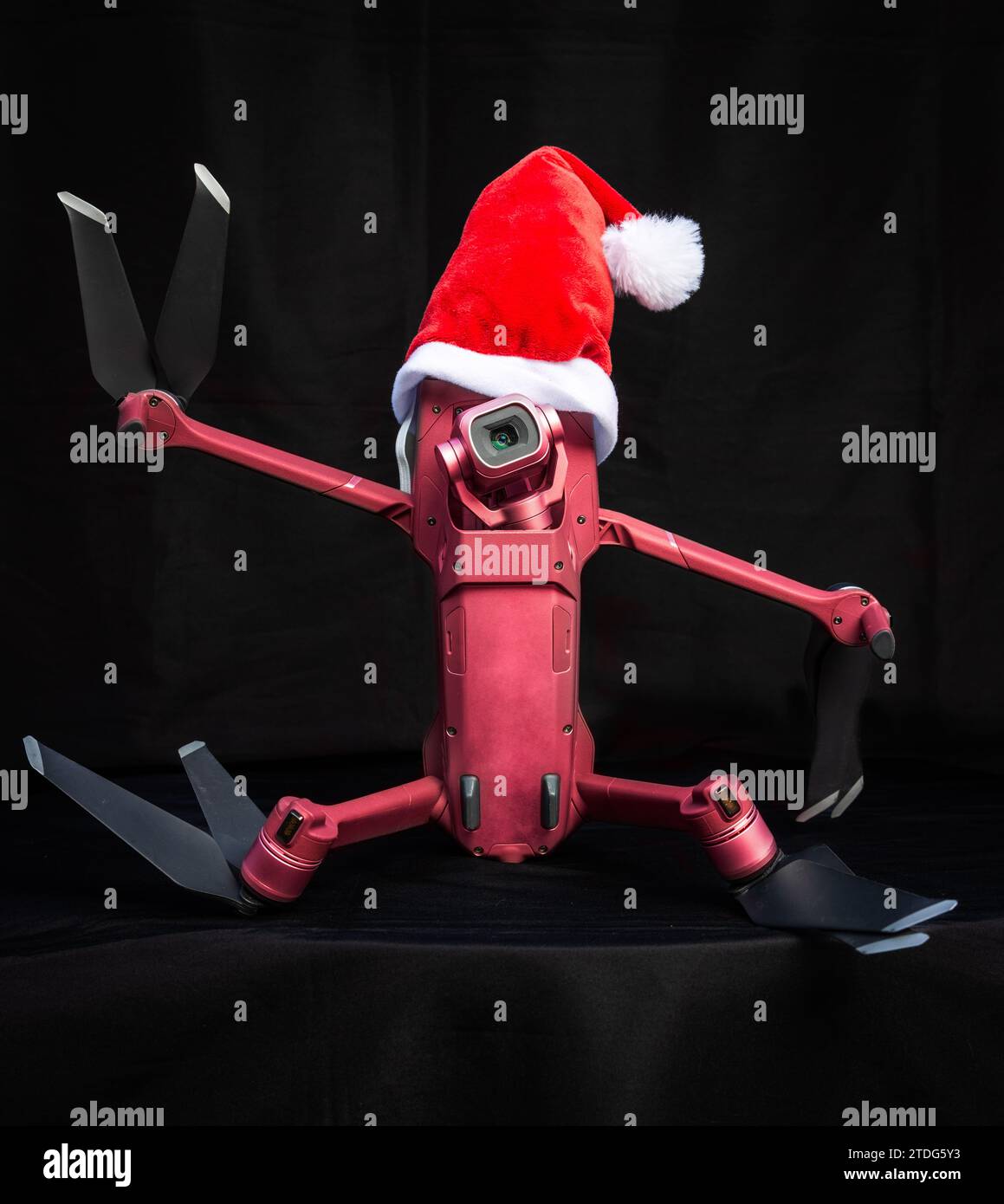 Porträt einer Quadcopter-Drohne mit weihnachtsmütze als Weihnachtskonzept auf dunklem Hintergrund, der das Friedenszeichen gibt. Stockfoto