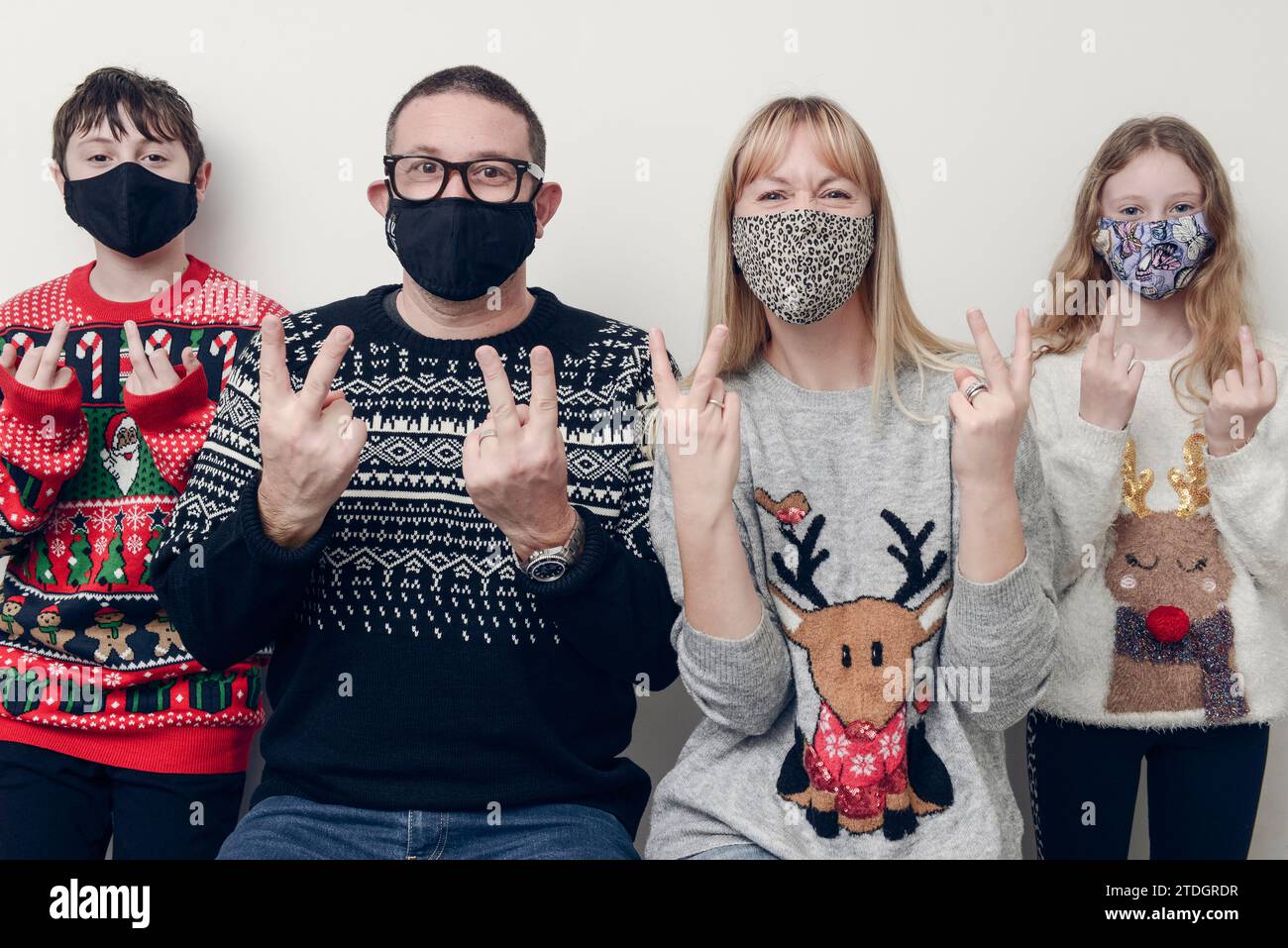 Eine Familie macht ein COVID-Weihnachtsfoto mit Weihnachtspullover und Gesichtsmasken vor weißem Hintergrund. Stockfoto