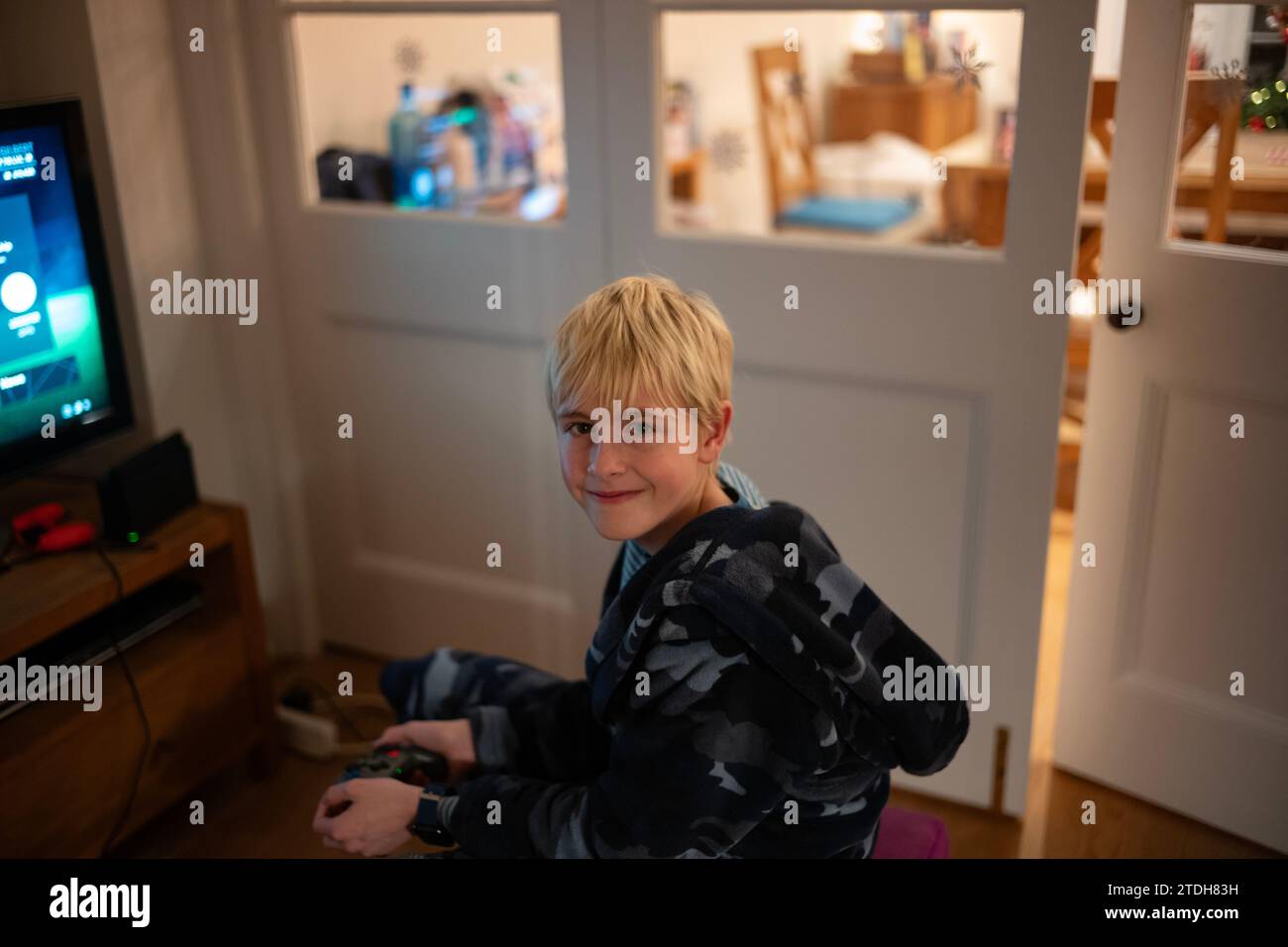 Ein Teenager im Morgenmantel lächelt in die Kamera, während er in seinem Wohnzimmer Nintendo spielt Stockfoto