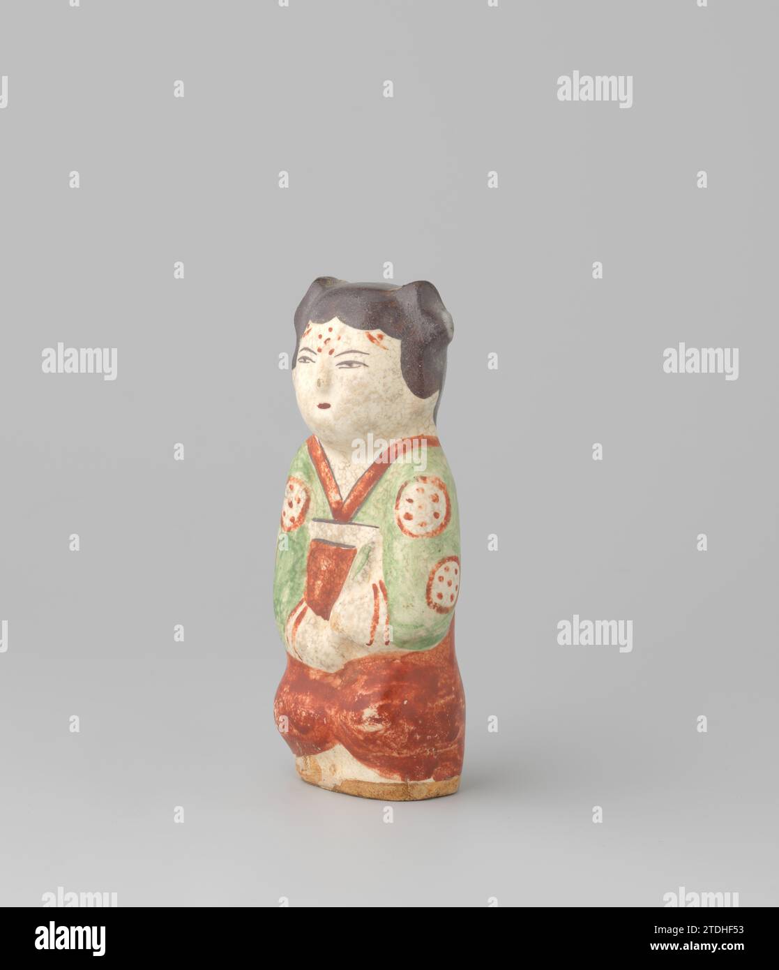 Lady, anonym, 1279 - 1368 die Dame ist, mit etwas in ihren Händen, vielleicht ein Fan. Ihr schwarzes Haar ist mit zwei roten Haarnadeln in zwei Brötchen gesteckt. Ihre Stirn ist mit einer Rosette aus fünf roten Punkten verziert. Sie trägt ein rot gesäumtes grünes Gewand mit einem Muster aus weißen Medaillons und roten Punkten sowie eine rote Schürze, deren weißes Band in eine Schleife auf dem Rücken gebunden ist. Porzellan Keramik Verglasung / Malerei die Dame ist, mit etwas in ihren Händen, vielleicht ein Fan. Ihr schwarzes Haar ist mit zwei roten Haarnadeln in zwei Brötchen gesteckt. Ihre Stirn ist mit einer Rosette aus fünf roten Punkten verziert. Sie ist wea Stockfoto