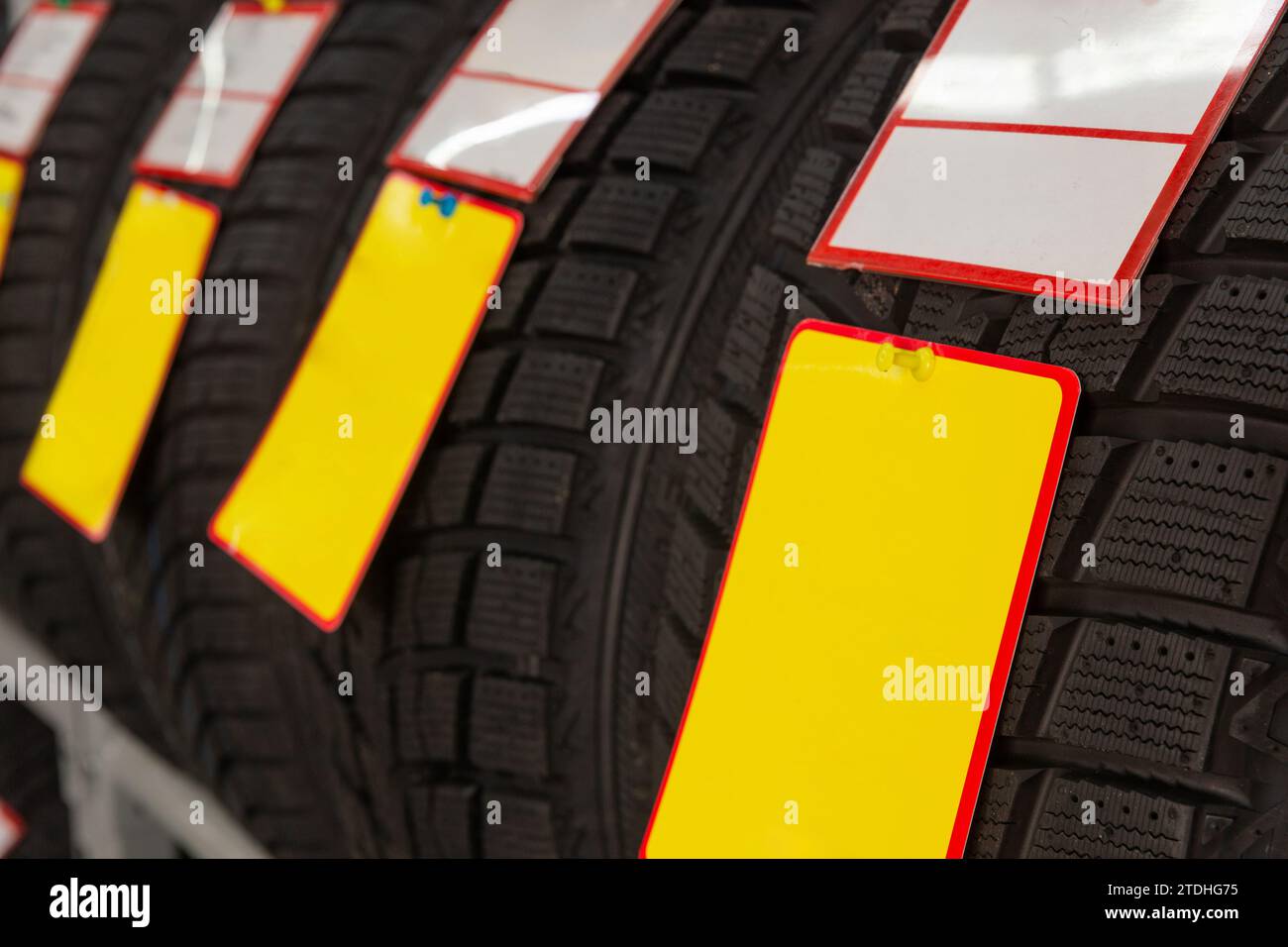 Winterreifen mit sauberen Hinweisschildern in einem Fachgeschäft. Nahaufnahme von neuen Reifen mit unbelegten Formularen, die mit Schreibwarenstiften fixiert sind. Stockfoto