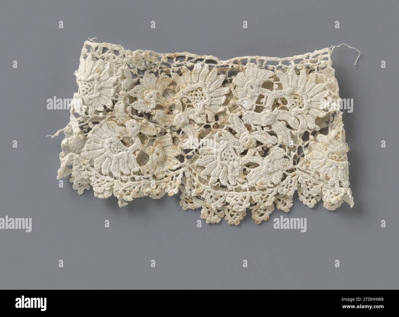 Manschette von der Häkelseite mit fächerförmigen Blüten, anonym, ca. 1890 - ca. 1909 Manschette aus natürlicher irischer Häkelseite, Nachahmung grober venezianischer Seite. Muster mit fächerförmigen Blüten mit Stielen und gehäkeltem unregelmäßigem Netzboden mit Pikots. Die Oberseite ist mit einem Lineal versehen. Die halbkreisförmigen Skulpturen am unteren Rand sind mit pikotierten Bögen versehen. Irische Baumwolle (Textil) Manschette aus natürlicher irischer Häkelseite, Nachahmung grober venezianischer Seite. Muster mit fächerförmigen Blüten mit Stielen und gehäkeltem unregelmäßigem Netzboden mit Pikots. Die Oberseite ist mit einem geraden edg versehen Stockfoto