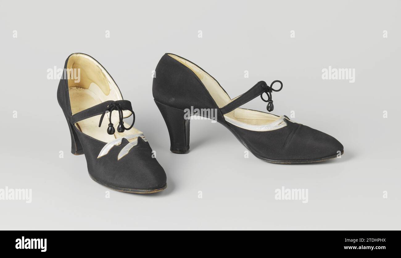 High-Heels-Schuhe mit gewellten Bändern, anonym, ca. 1930 Damenschuh aus schwarzem Satin. Modell: Abgerundete Nase, ein Deckblatt und zwei Seitenbleche. Die Seitenbleche und die Deckblätter kommen am Geleng zusammen. Von diesem Punkt an laufen zwei Reifen über den Riegel. Die Reifen werden durch ein schwarzes Seil mit schwarzer Wulst zusammengehalten. Die Vorderseite der Ferse verläuft in einem abgerundeten Winkel gerade nach unten. Die Seite und Rückseite der Ferse sind leicht geschnitten und mit schwarzem Satin bedeckt. Achlap aus schwarzem Leder mit fünf Nägeln an der Ferse und schwarzer Ledersohle. Mit elfenbeinfarbenem weißem Leder gefütterte Seitenlaken. Abdeckung Stockfoto