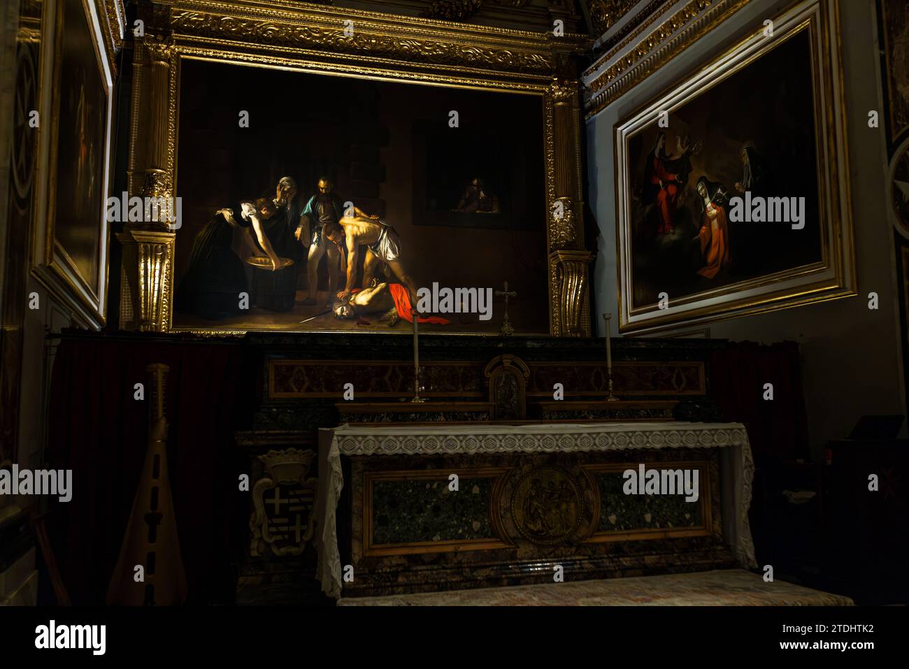 Caravaggios Altarbild „Die Enthauptung des heiligen Johannes des Täufers“ (1608) hängt über dem Altartisch der Oratoriumskirche der Konkathedrale St. Johannes in Valletta, Malta; rechts davon hängt sein Gemälde „Der heilige Hieronymus beim Schreiben“ (ca. 1607–08), das den Kirchenvater bei der Arbeit an seiner Bibelübersetzung zeigt. Die Enthauptung ist das einzige Gemälde, das Caravaggio jemals signierte: er schrieb seinen Namen in das Blut, das aus dem abgetrennten Hals des Täufers fließt. Der Orden von St. Johann ließ die Kathedrale zwischen 1572 und 1577 erbauen; ihr reich vergoldetes Inneres stammt größtenteils aus den 1660er Jahren und später durch die Arbeit von Mattia Preti. Stockfoto
