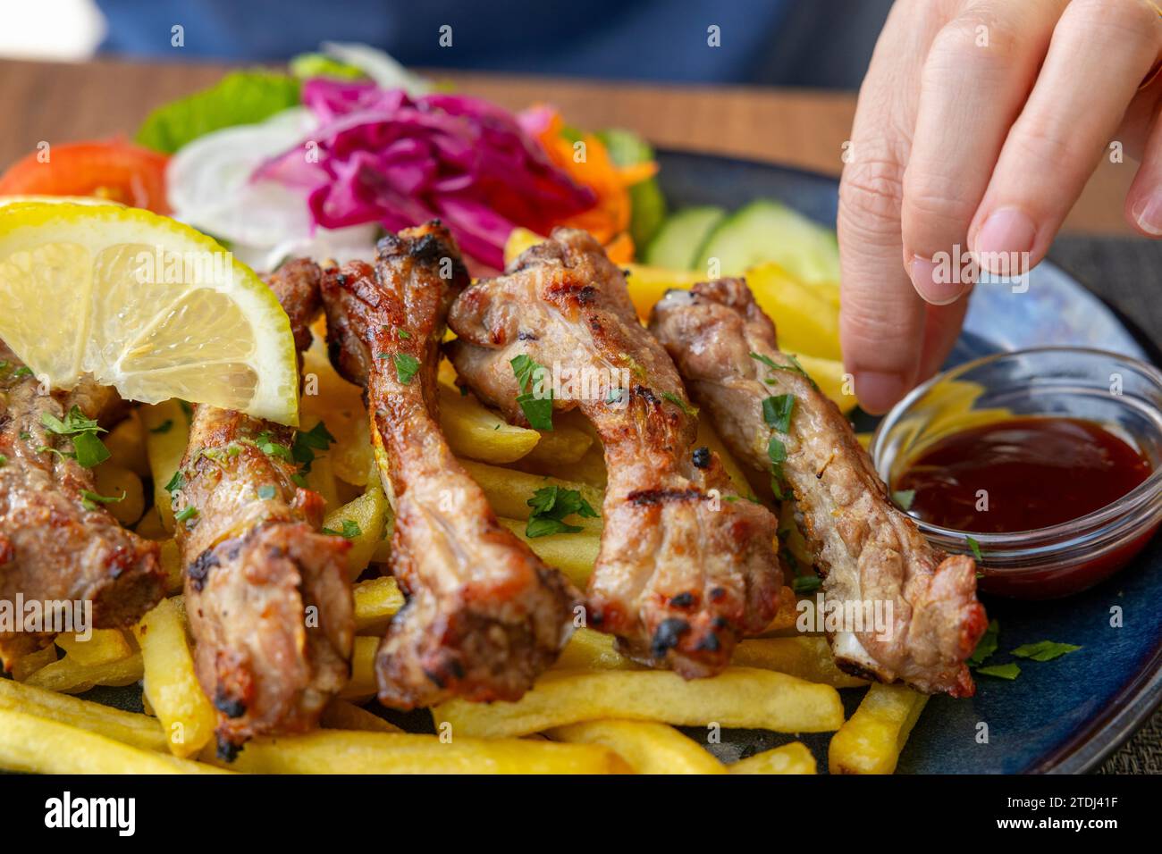 Nahaufnahme des Tellers mit gegrillten Sparerippchen mit Pommes frites und Salat mit weiblicher Hand Stockfoto