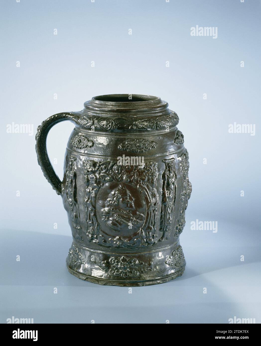 Tankard mit Porträts, Schriftrollen und Blattornamenten, anonym, ca. 1620 Bierbecher aus Steingut auf leicht ausbreitendem Fuß und mit leicht eiförmigem Körper. Das C-förmige Ohr ist an einem Profil unter der Kante und am Bauch befestigt. Bedeckt mit einer braunen Engobe. Auf dem Bauch im Relief drei gedruckte und auferlegte Rollen und Putten, getrennt durch Karyatiden. In den Kursen in einem Medaillon ein geflügelter Engelskopf und eine Dame und ein Gentleman und Profil. An der Fußschulter und -Kante ein Riemen mit Locken- und Blattmotiven. Creusen. Creusener Steingut. Glasur. Engobe Vitrification Bierkrug aus Steinholz Stockfoto