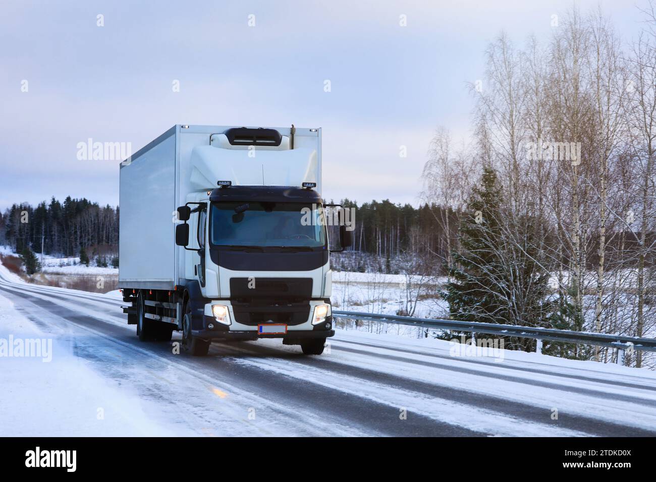 Weißer, gekühlter Lieferwagen transportiert an einem bewölkten Wintermorgen auf der Autobahn. Stockfoto
