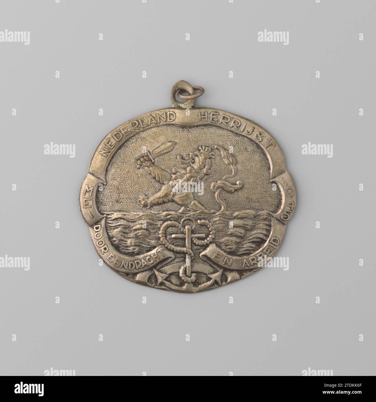 Anhänger „The Netherlands Rises“ mit Drahtrahr, 1945 Anhänger oder Brosche „The Netherlands Rises“ mit Drahtrahr. Entlang der leicht gewellten Kante verläuft eine Banderole, die von einem Anker am Boden unterbrochen wird. Am Horizont erhebt sich der niederländische Löwe aus dem Meer. Niederlande Metallanhänger oder Brosche „The Netherlands Rises“ mit Drahtelöse. Entlang der leicht gewellten Kante verläuft eine Banderole, die von einem Anker am Boden unterbrochen wird. Am Horizont erhebt sich der niederländische Löwe aus dem Meer. Niederlande Metall Stockfoto