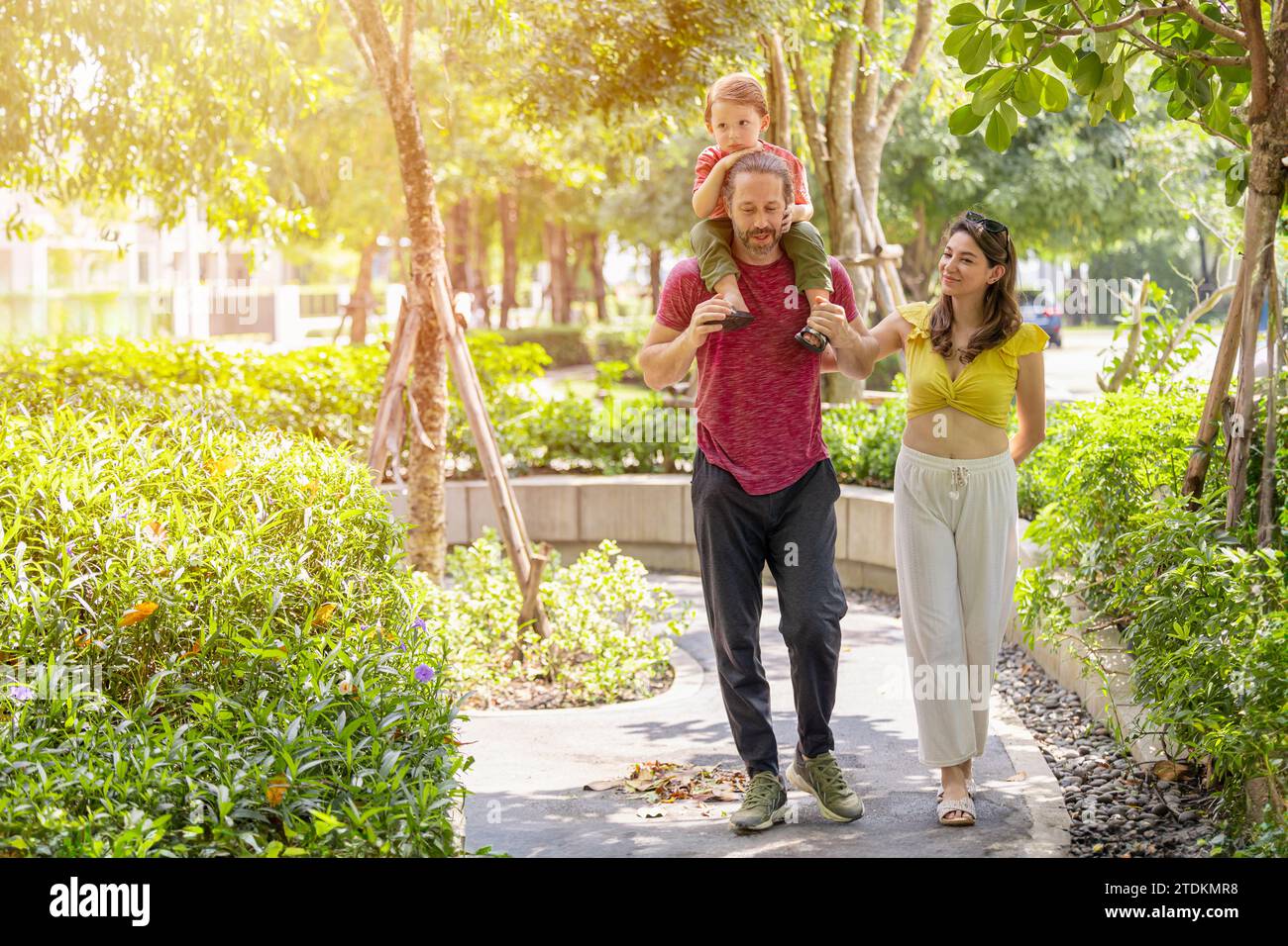 Glückliche Familie zusammen spazieren im öffentlichen grünen Park junger Junge, der auf der Schulter des Vaters um frische ökologisches Bäume herum sitzt. Stockfoto