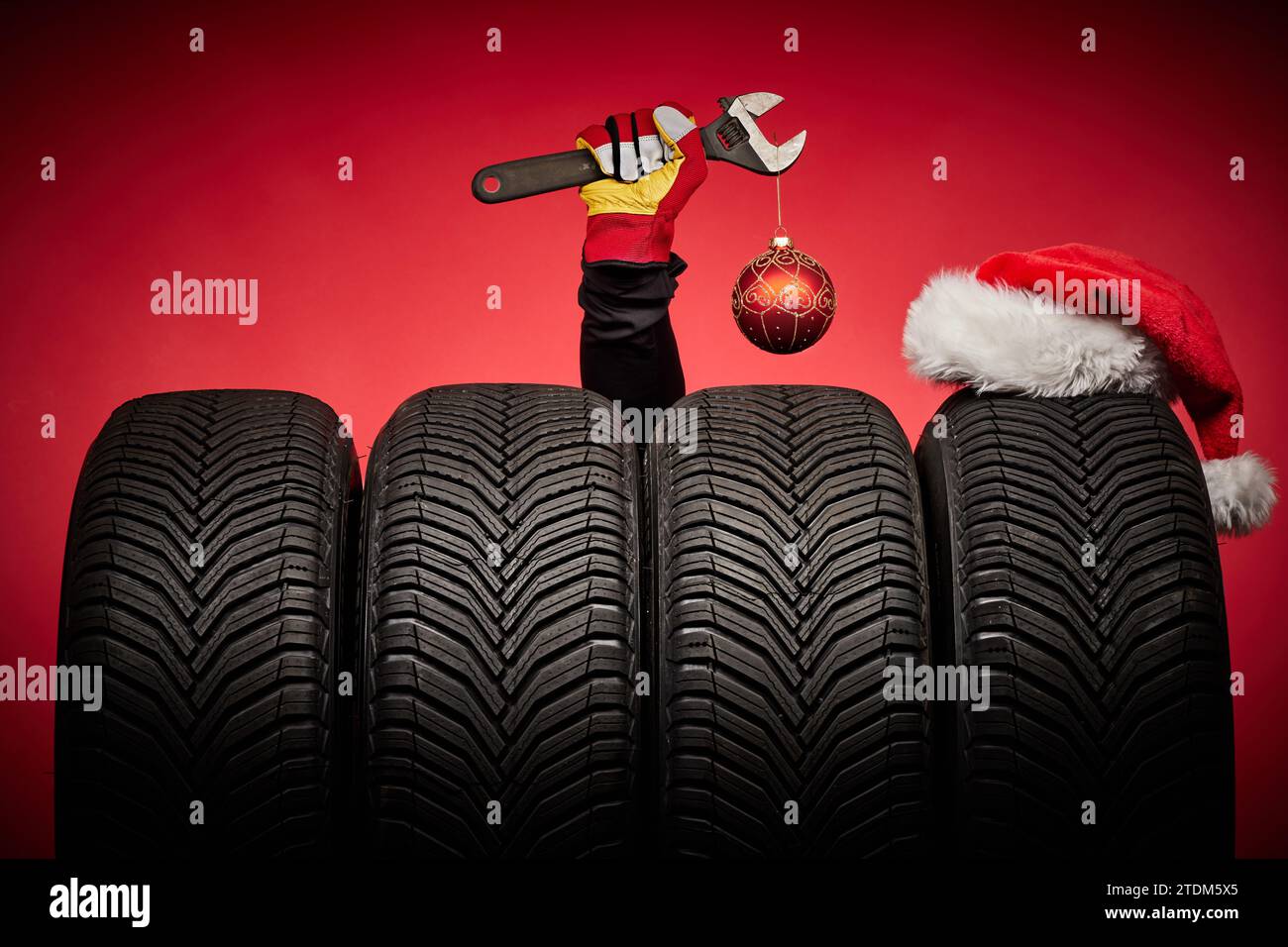 Winterreifen, große Räder, Reifen, Mechaniker Hand mit Schraubenschlüssel, weihnachtsbaumkugel und Weihnachtsmann Hut auf rotem Hintergrund. Stockfoto