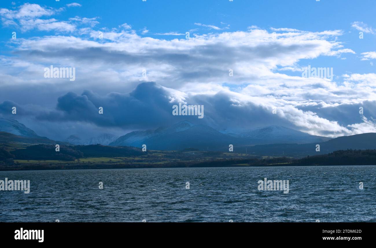 Ein Wintersturm zieht über die Berge von Snowdonia und legt eine Schneeschicht ab. Der Blick über die Menai Straights trägt zum Gefühl der Skala bei. Stockfoto