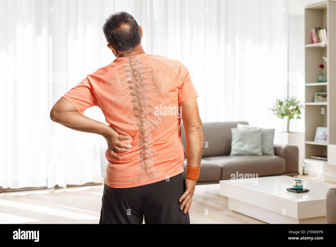 Rückansicht eines Mannes, der seinen schmerzhaften Rücken in einem Wohnzimmer mit sichtbarer Wirbelsäule hält Stockfoto