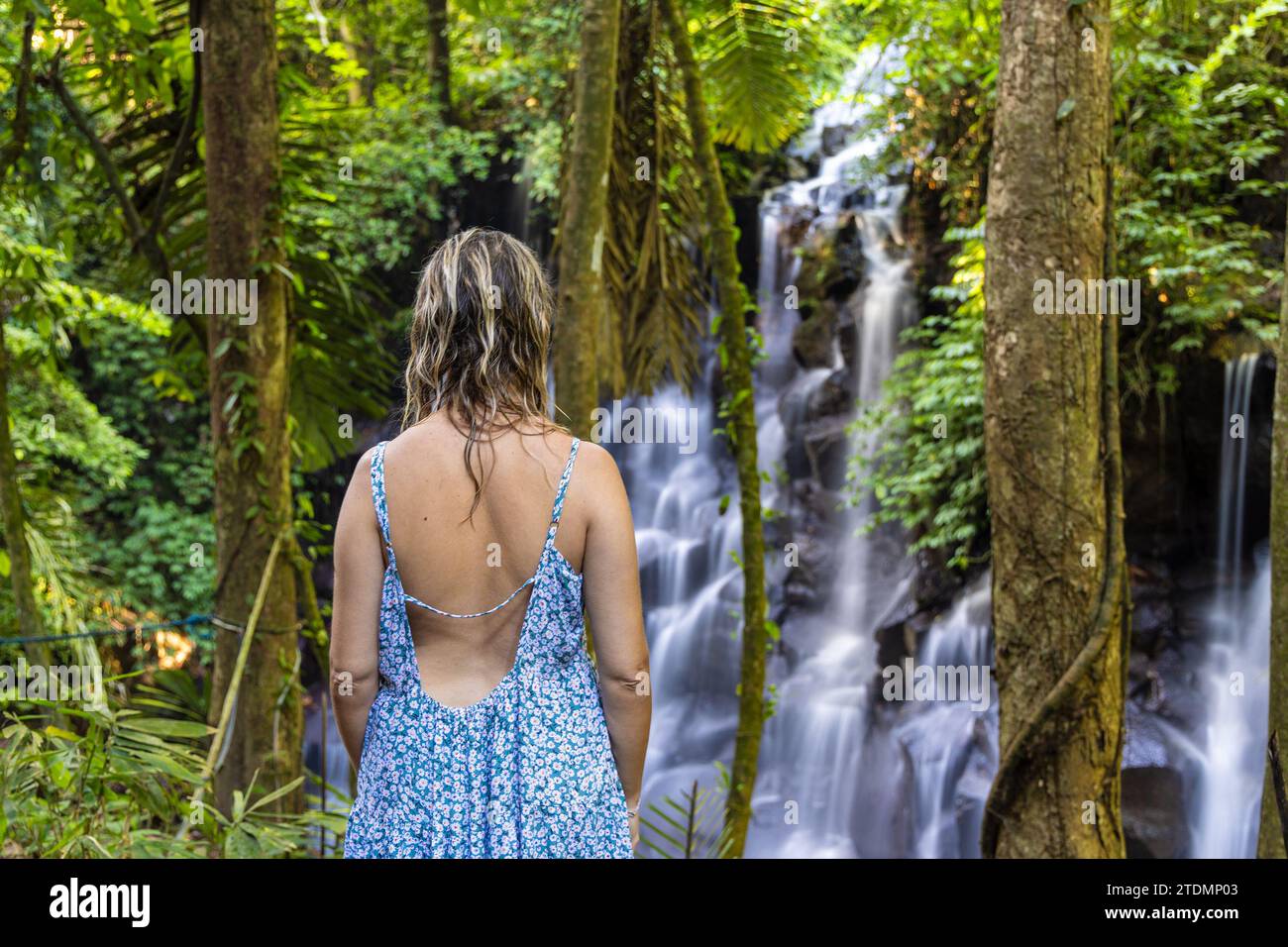 Eine junge Frau in einem Kleid am Kanto Lampo Wasserfall im üppigen tropischen Wald, Bali, Indonesien Stockfoto