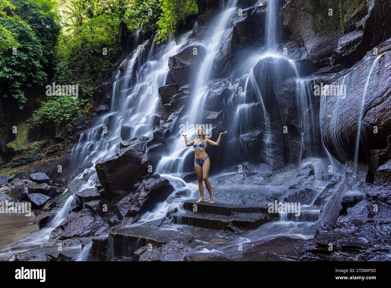 Eine junge Frau im Badeanzug am Kanto Lampo Wasserfall im üppigen tropischen Wald, Bali, Indonesien Stockfoto