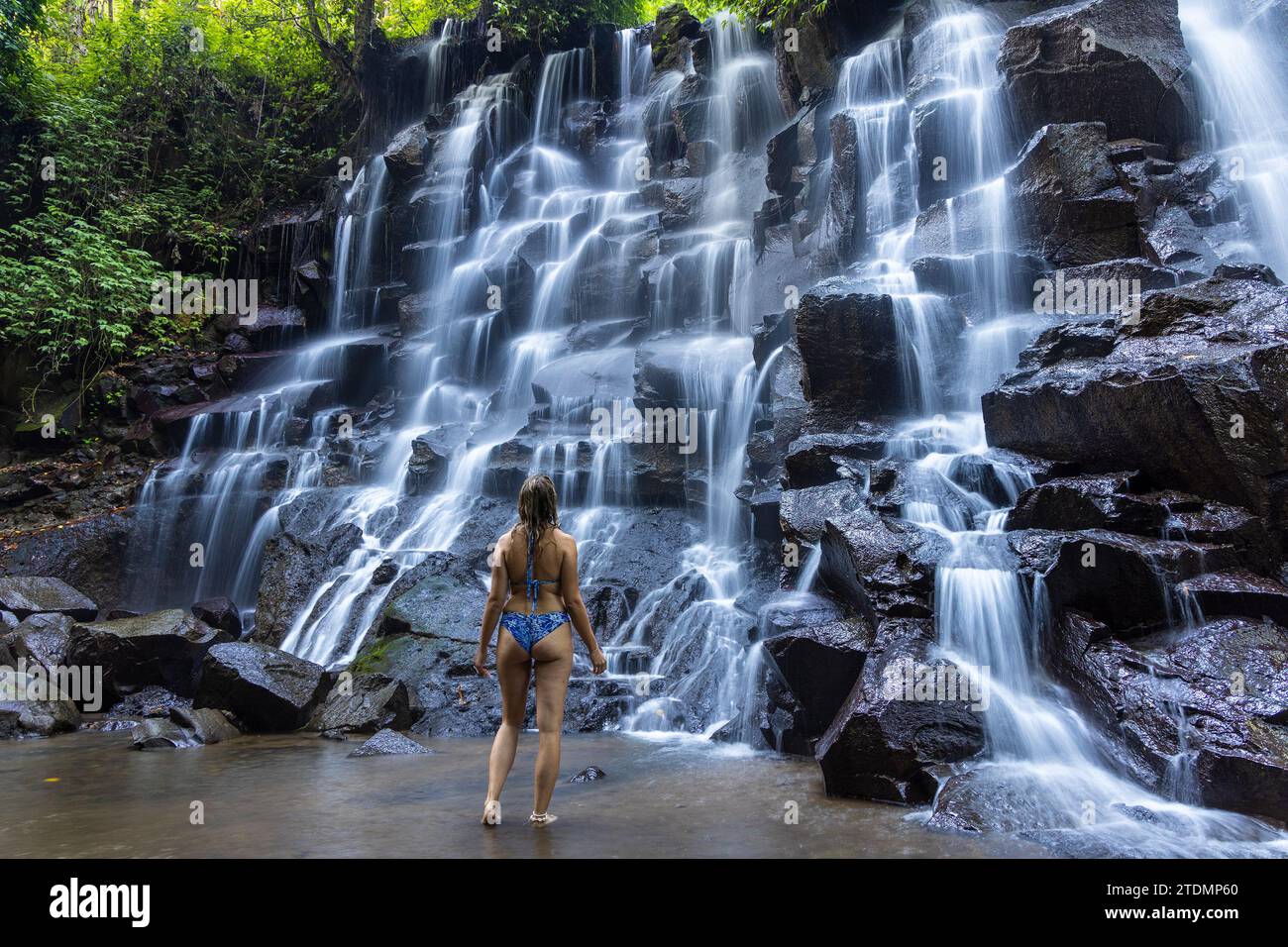 Eine junge Frau im Badeanzug am Kanto Lampo Wasserfall im üppigen tropischen Wald, Bali, Indonesien Stockfoto